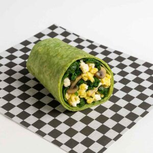 A hyper-realistic image of a Greek Wrap made with a spinach tortilla, scrambled eggs, fresh spinach, mushrooms, and feta cheese, served on black-and-white checkered deli paper against a clean white background. Perfect for anyone searching for a Greek Wrap or Breakfast near me in Newport News.