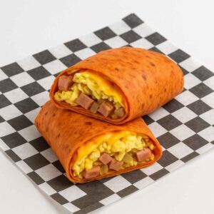A hyper-realistic image of a Southwest Wrap made with a sun-dried tomato tortilla, filled with scrambled eggs, diced ham, sautéed onions, and melted cheddar cheese, served on black-and-white checkered deli paper against a clean white background.